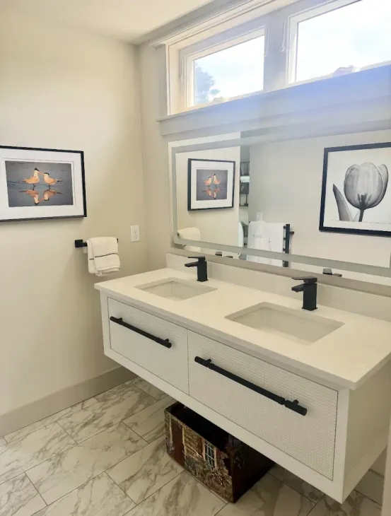 Bathroom with white double vanity, black fixtures, artwork, and large mirror.