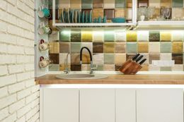 Kitchen with white brick wall, colorful tile backsplash, and wooden countertop over white cabinets.