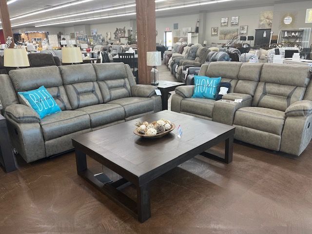 Living room furniture set: gray sofa, loveseat, coffee table, and decorations in a store.