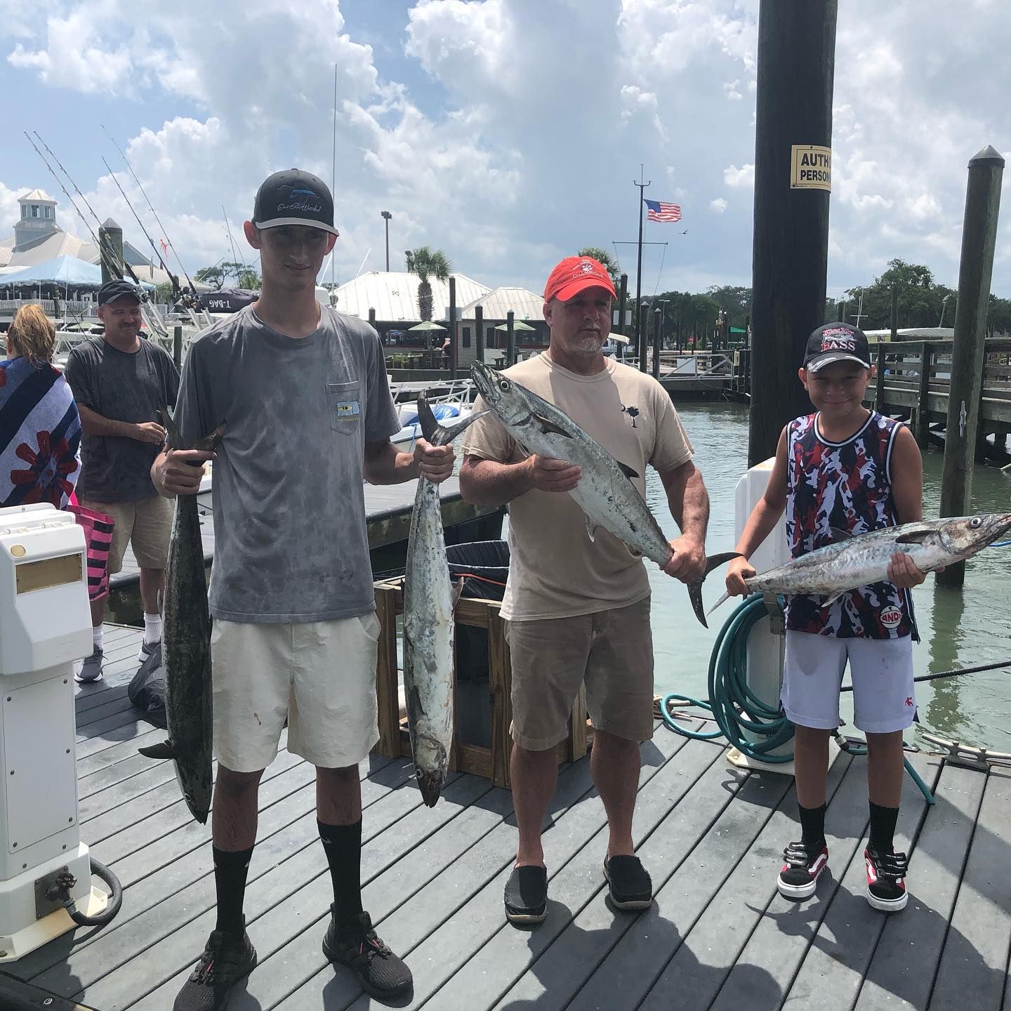 Four people on a dock holding fish, likely caught while fishing. Blue water, sunny day.