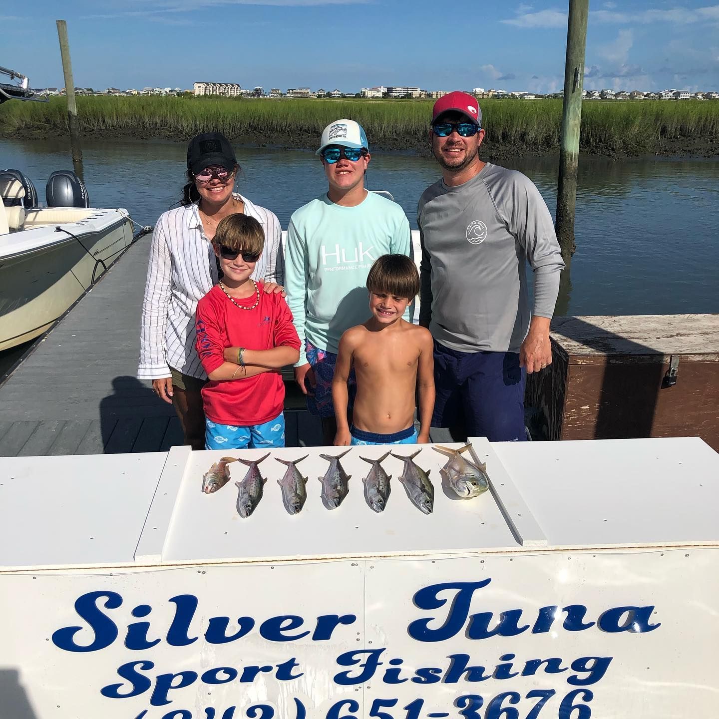 Family on a dock displays their fish catch in front of a 