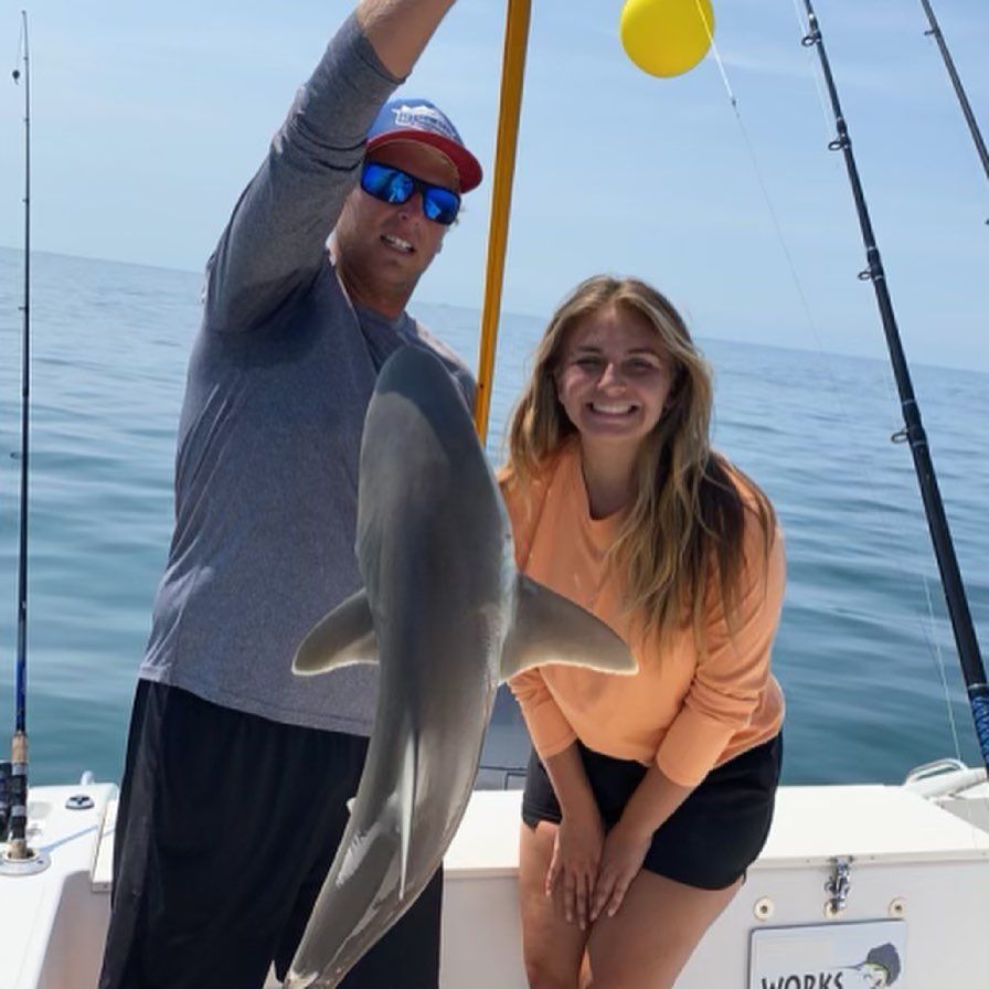 Man holding up dolphin next to woman smiling on a boat at sea.