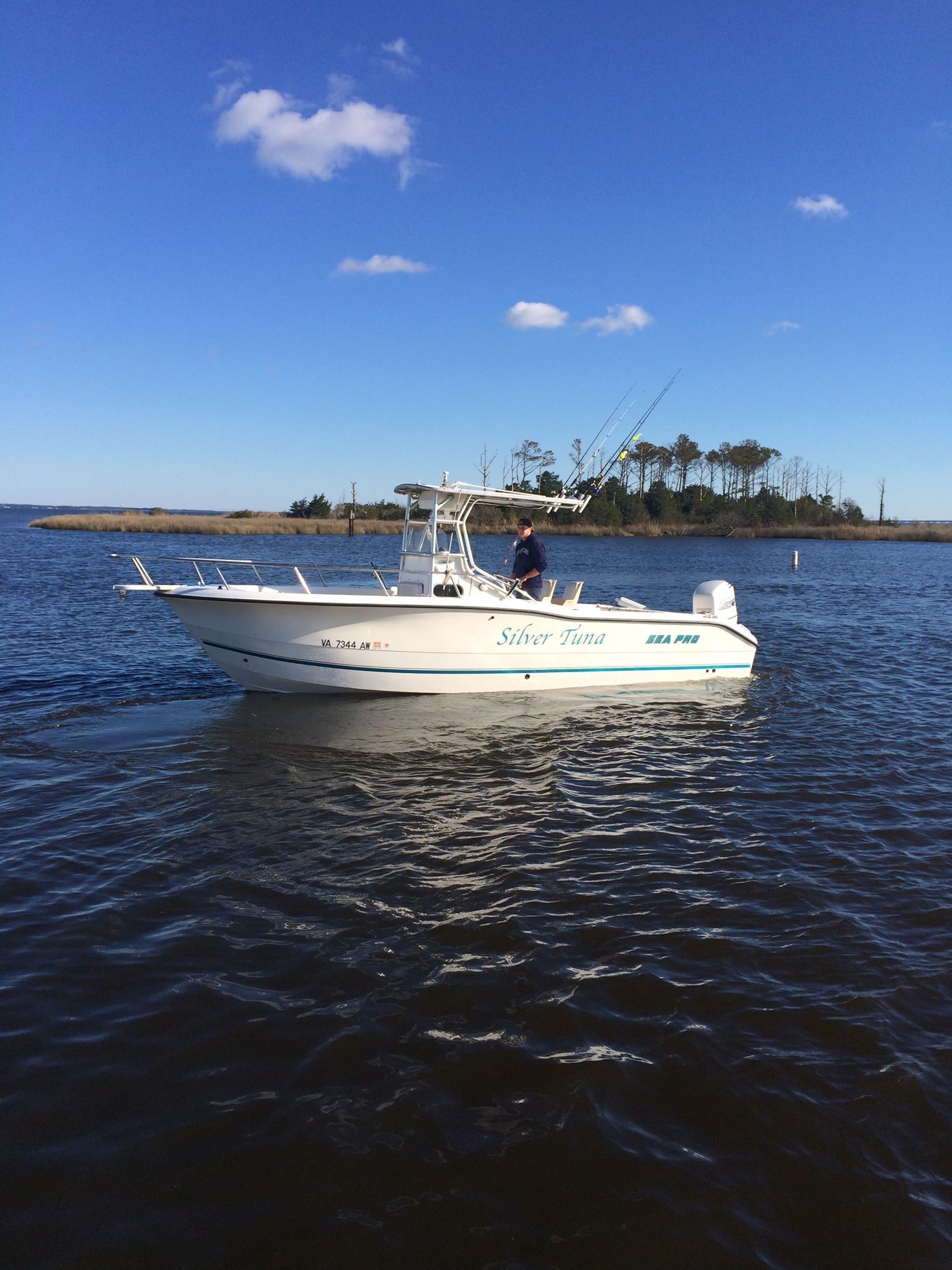 Fishing boat on calm water under a blue sky with a few clouds, near a treeline.