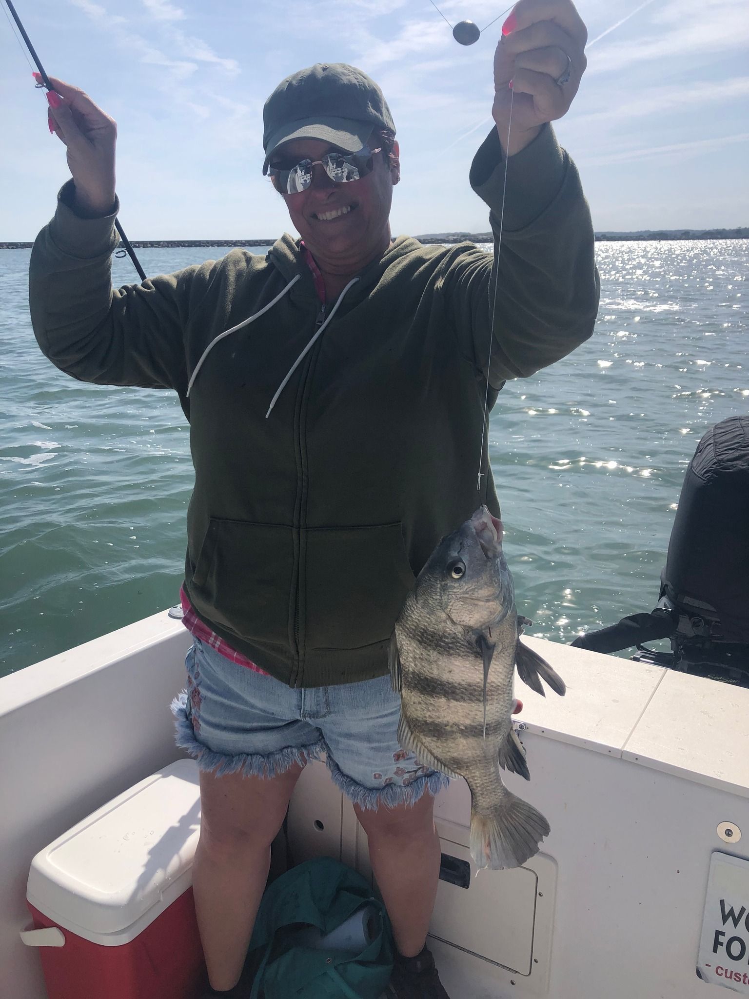 Woman on a boat, holding up a freshly caught striped fish, smiling. Outdoors, sunny day.