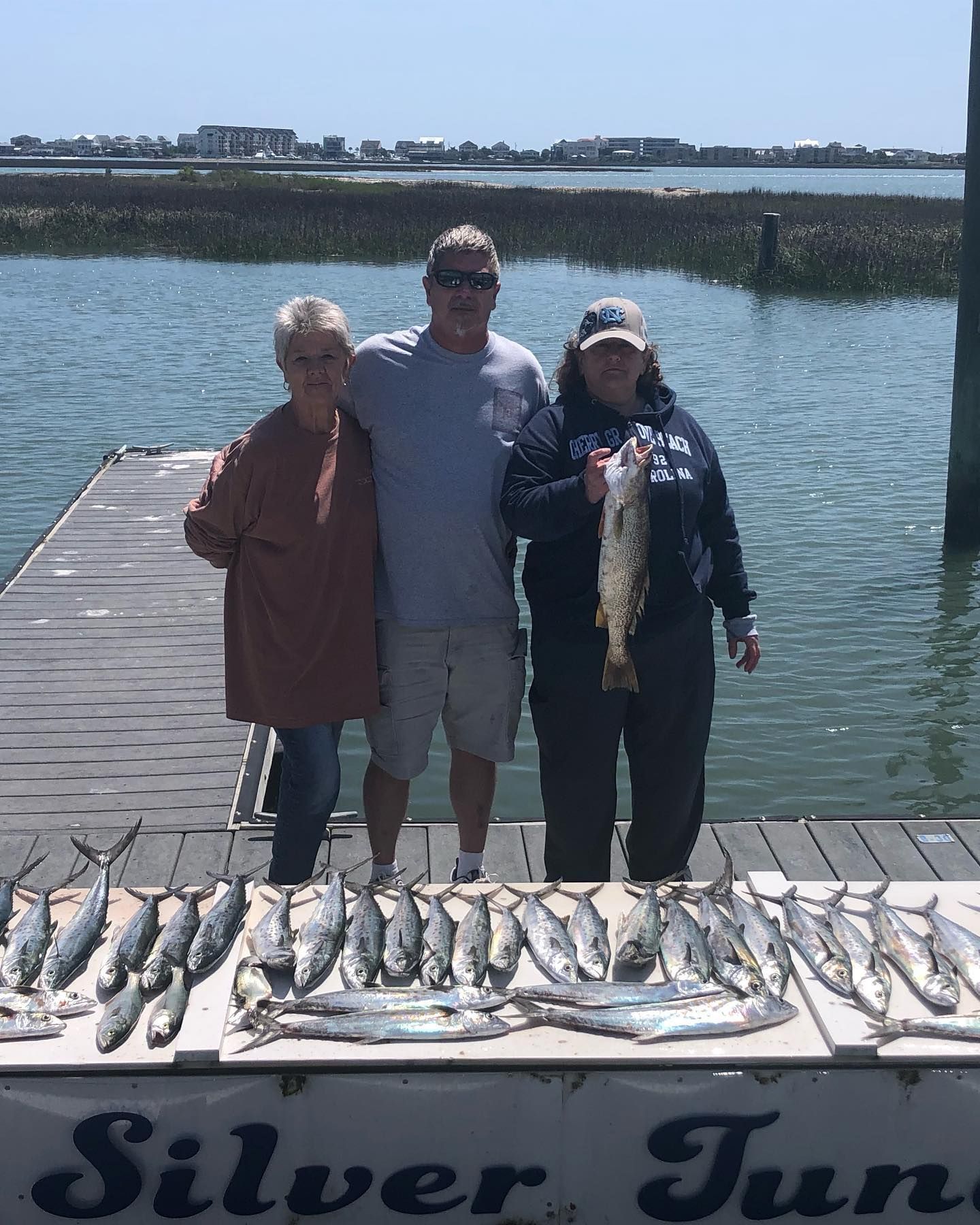 Three people on a dock with caught fish; woman holding a speckled trout.