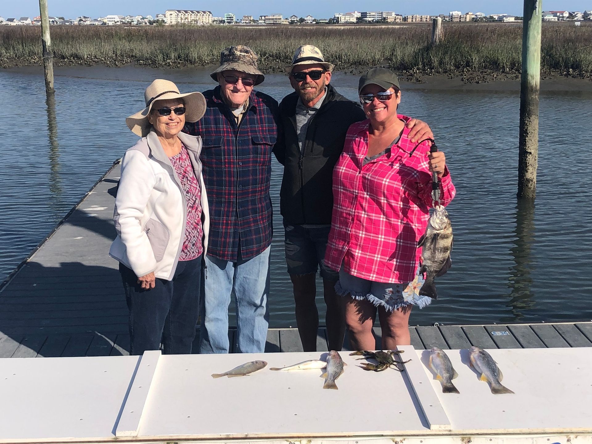 Four people on a dock, smiling with a fish catch displayed on a table in the sun.