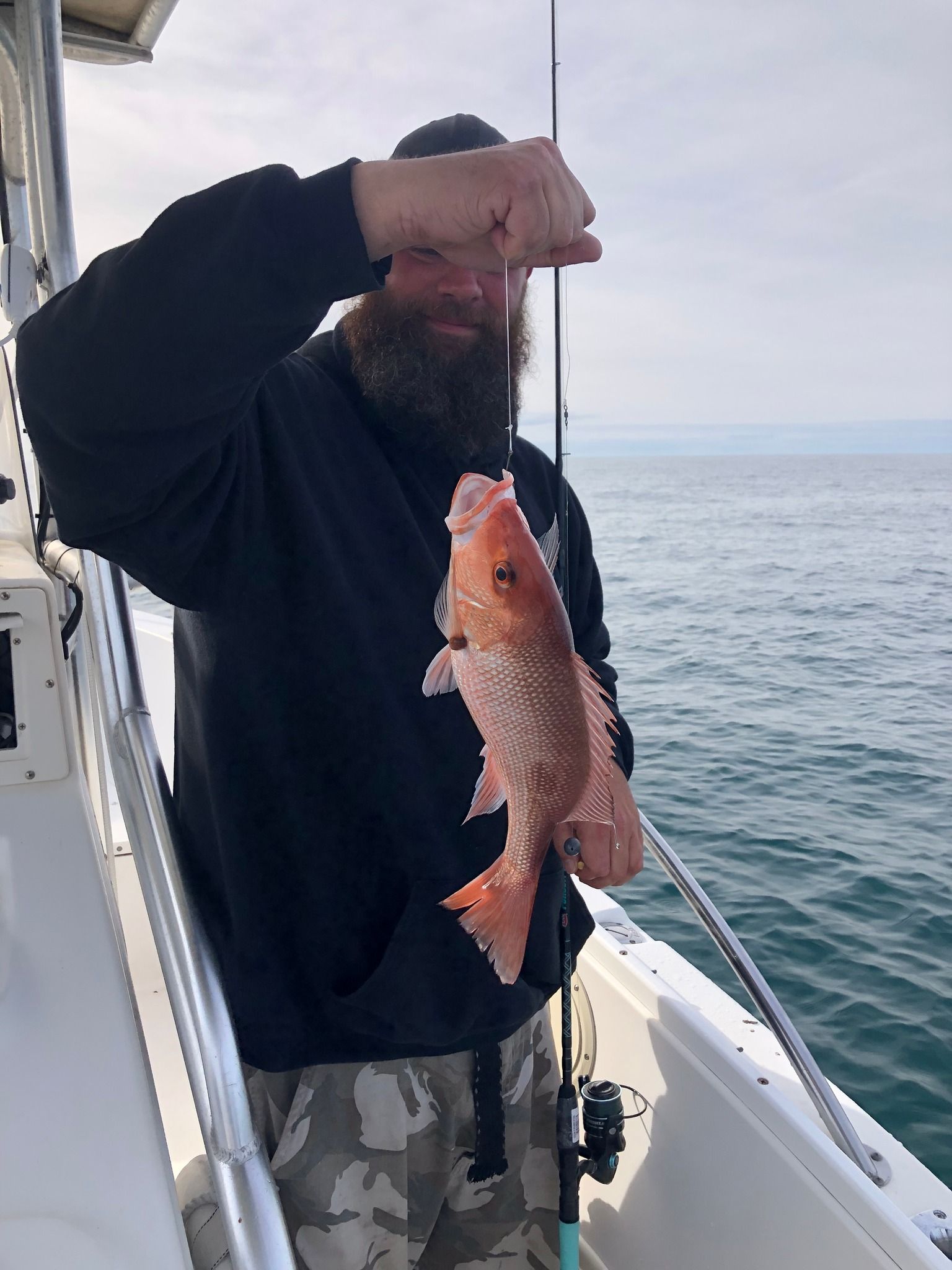 Man on boat holds up red fish; ocean in background.
