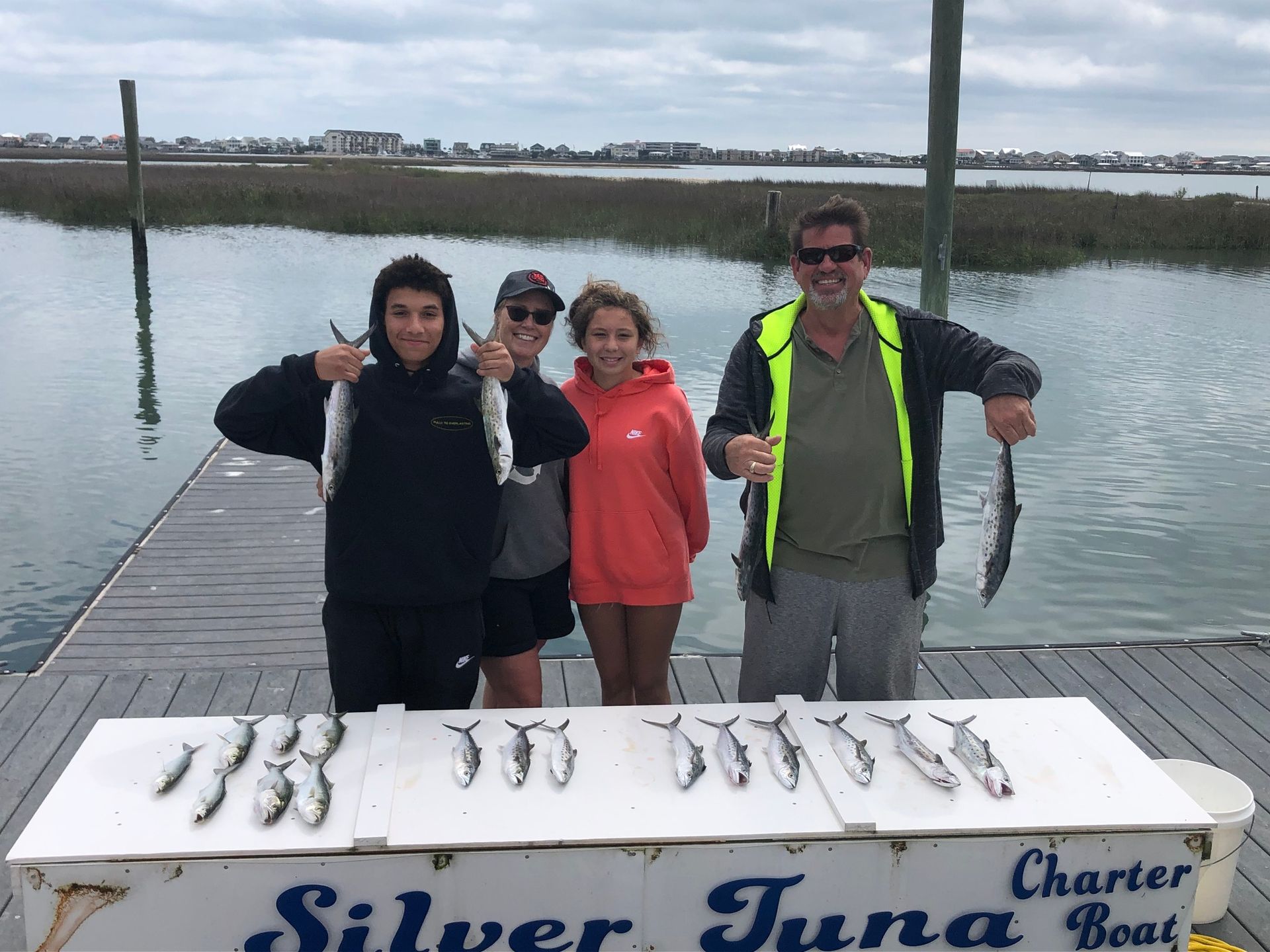 Family on dock with silver fish catch; cloudy day at sea.