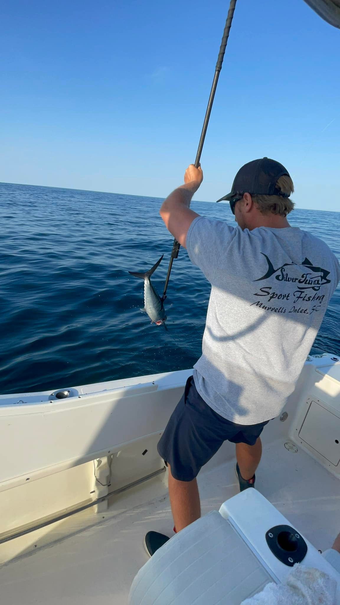 Man reeling in a small fish on a boat, sunny day, blue water.