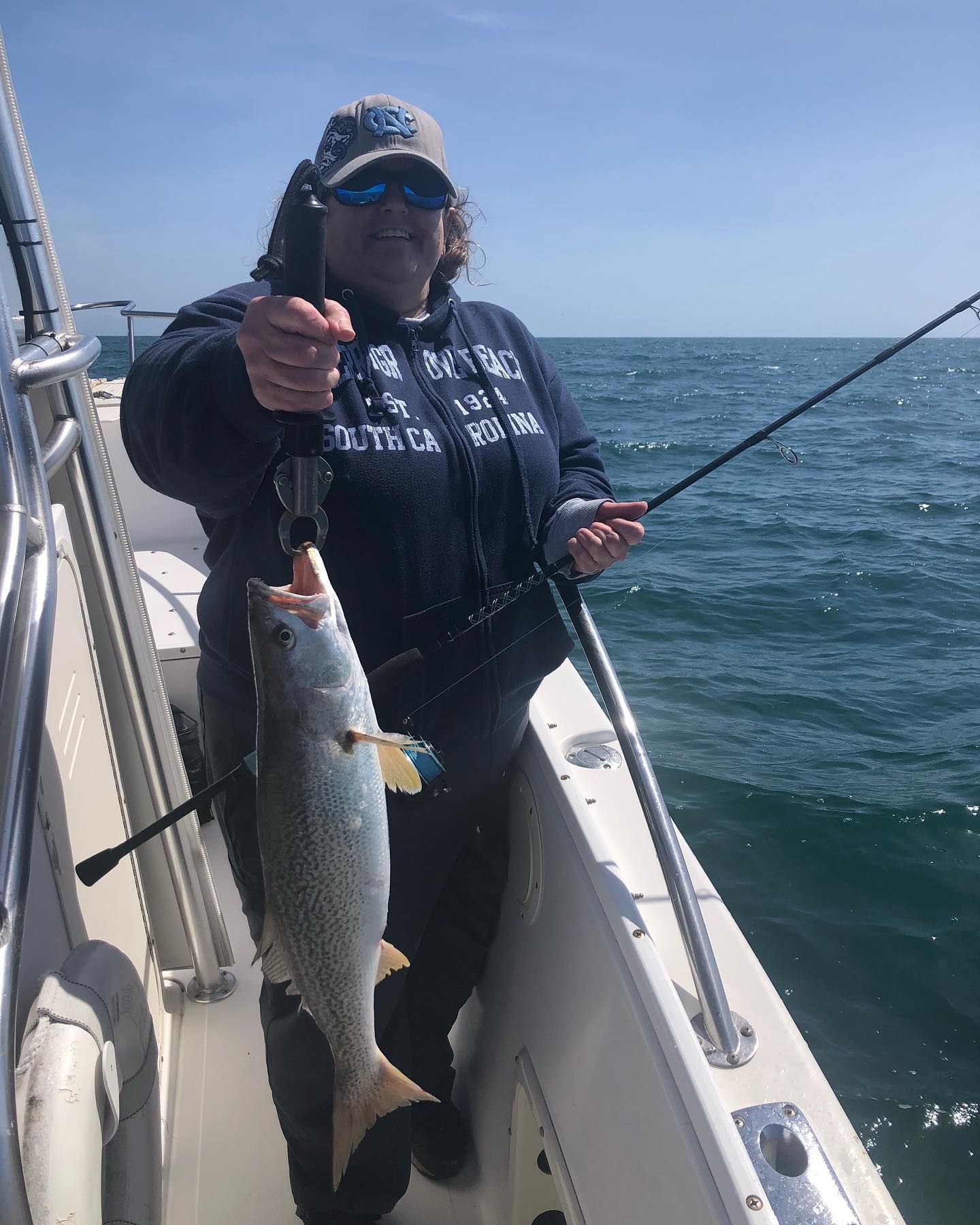 Woman on boat fishing, holding a speckled trout, sunny day on the water.