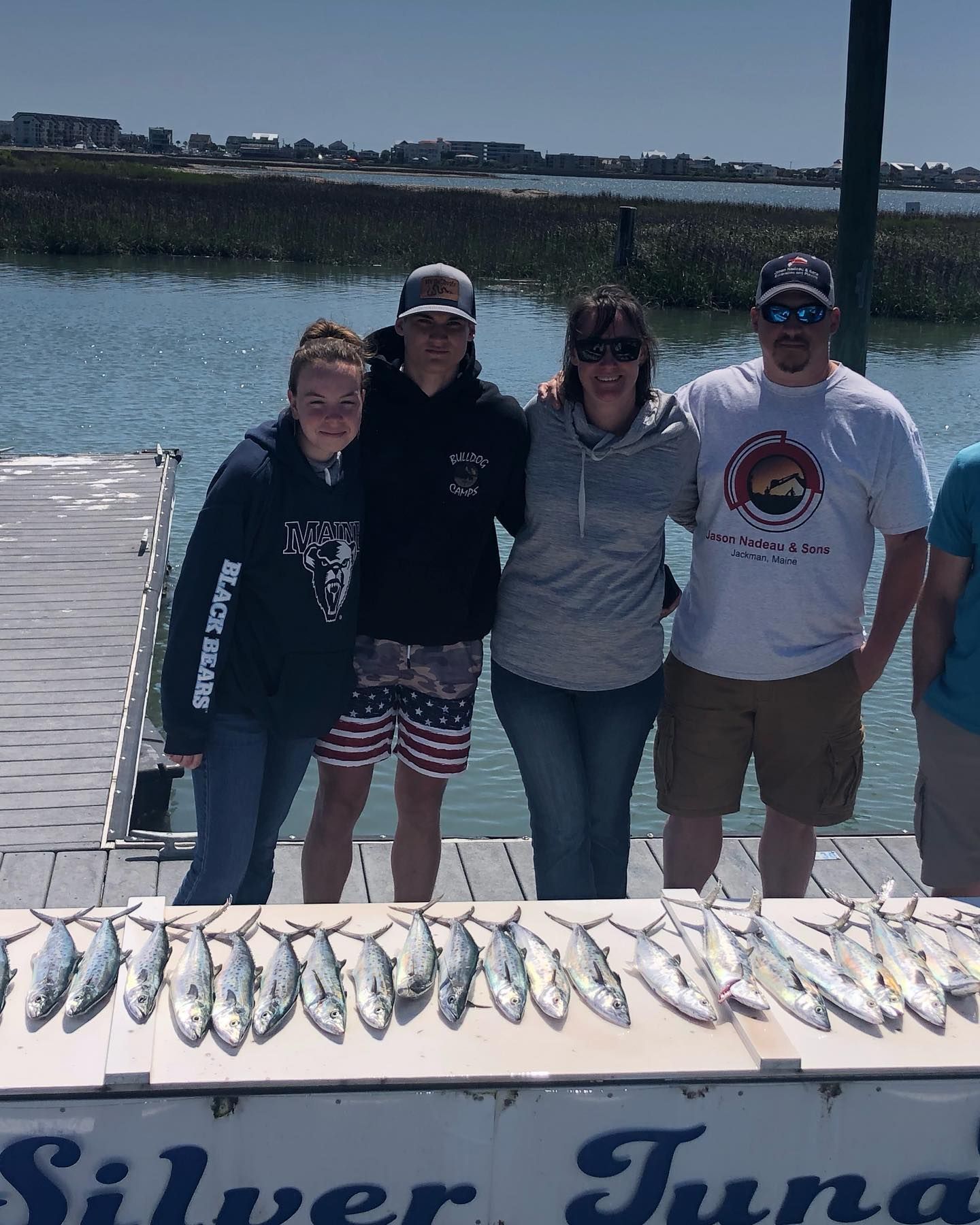Family on a dock with a large catch of fish; sunny day.