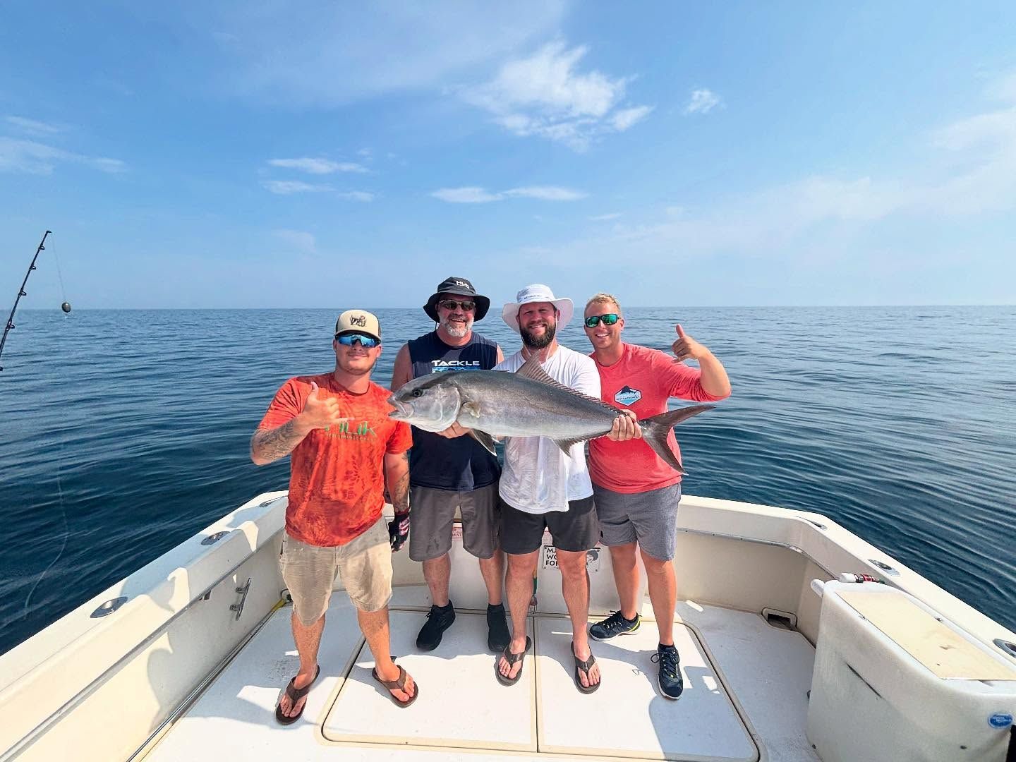 Four men on a boat, smiling, holding a large fish. Ocean and blue sky in the background.