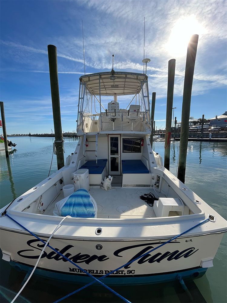 Four men on a boat, smiling, holding a large fish. Ocean and blue sky in the background.