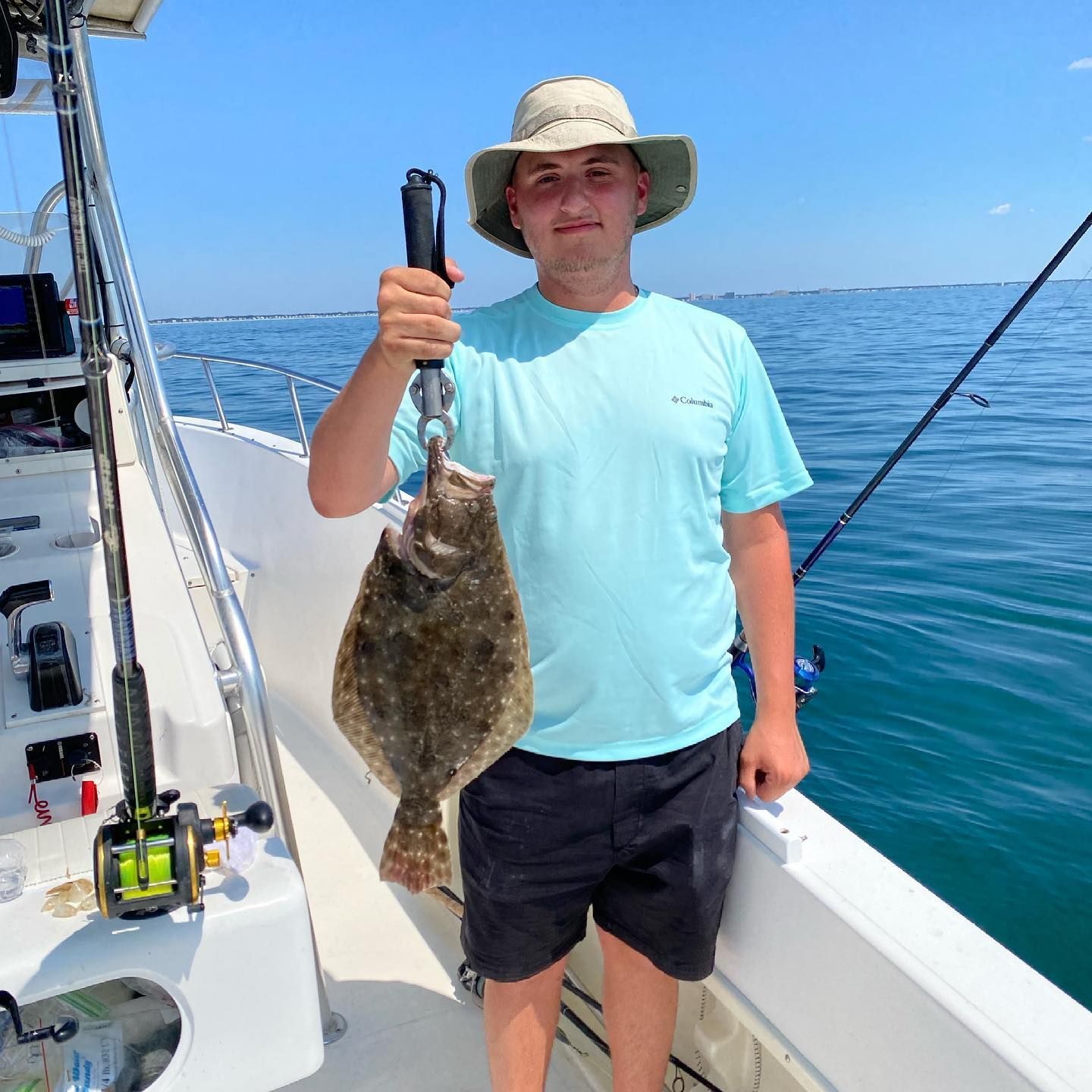 Man on boat holding a large flatfish, bright blue sky, sunny day.