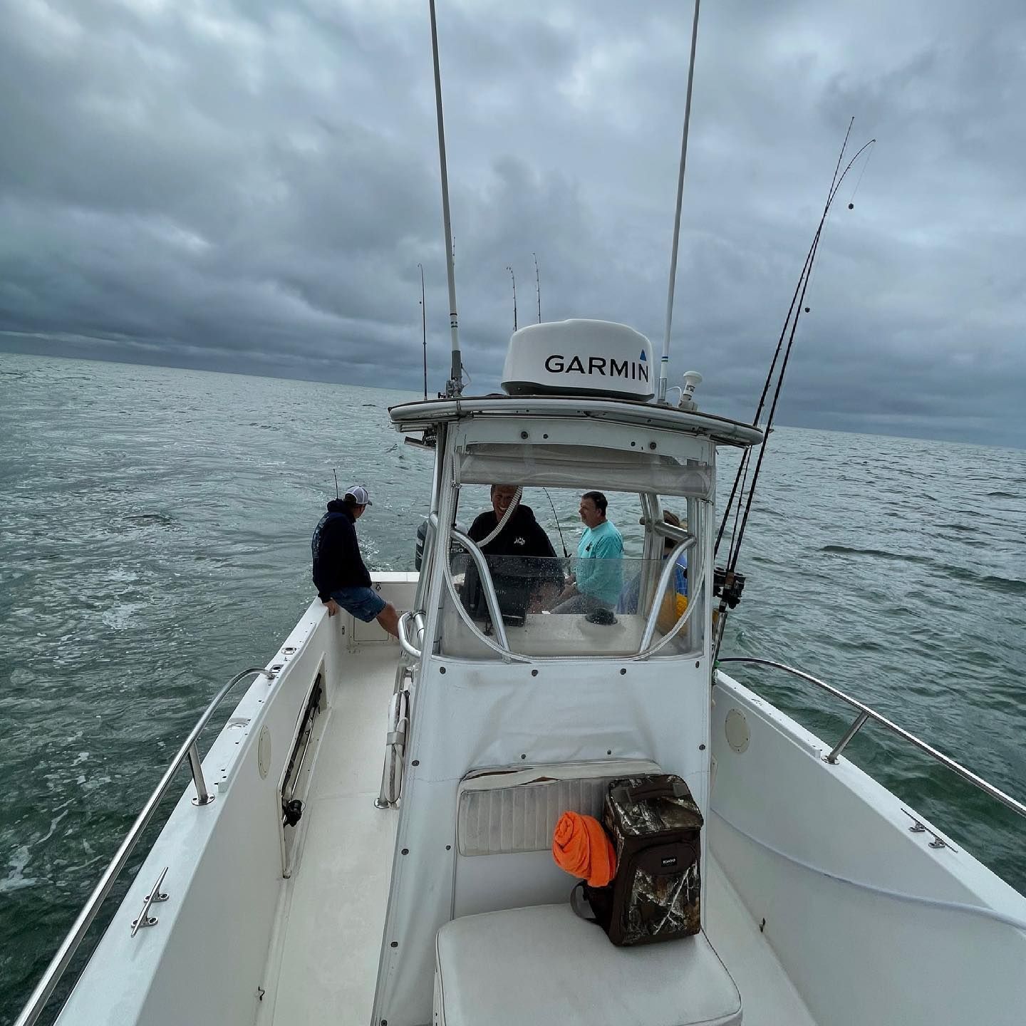 People fishing on a boat in the ocean under a cloudy sky.