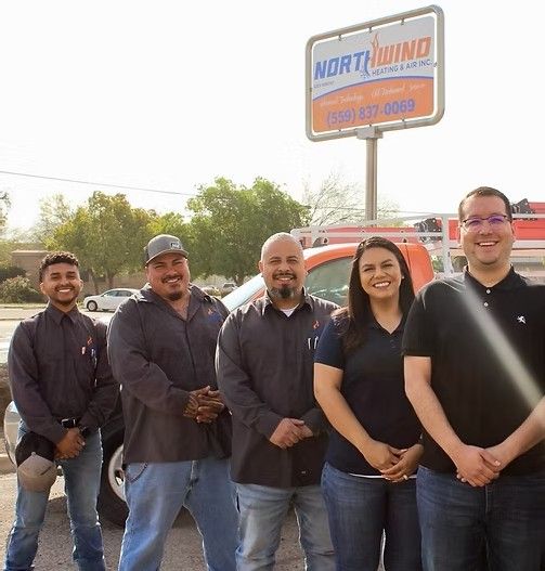 Five people pose smiling in front of a Northwind Heating & Air sign and a service truck.