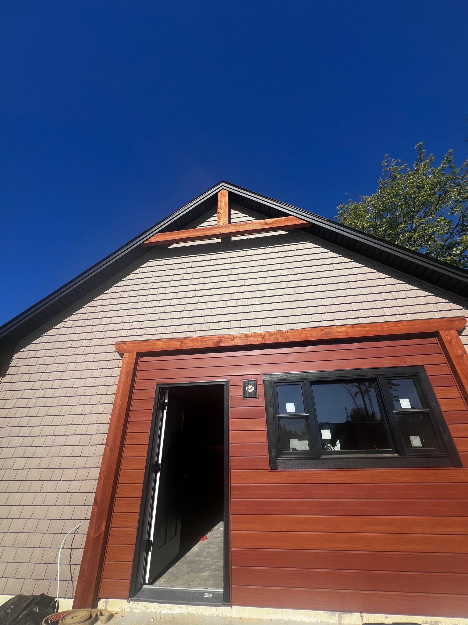 Exterior of a building with cedar wood trim and siding, a black-framed window and door, and a clear blue sky.