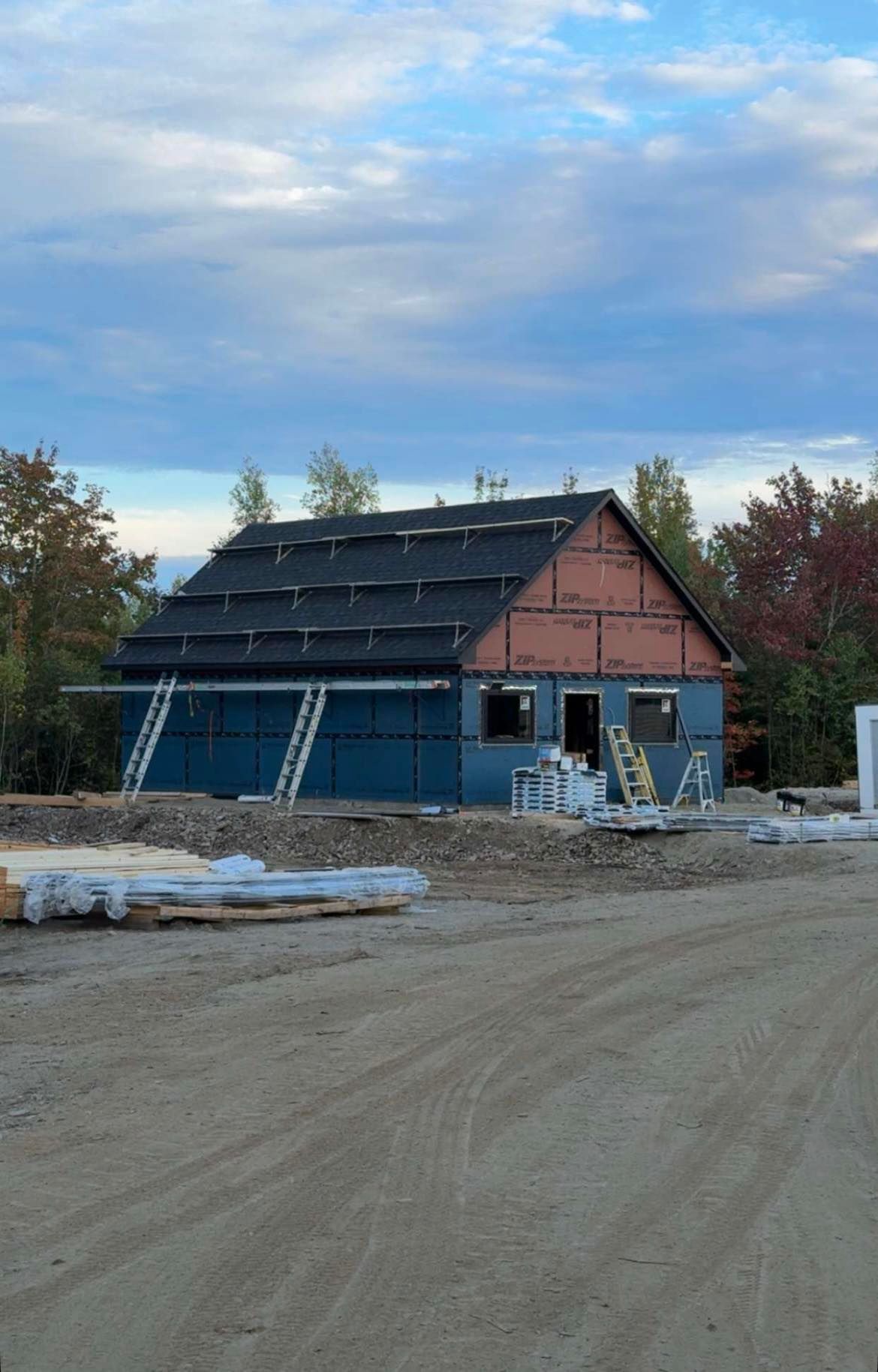 A building under construction with a dark roof and blue siding, surrounded by construction materials, under a cloudy sky.