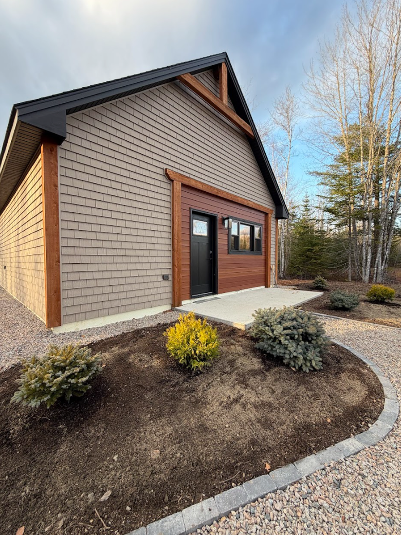 Exterior of a building under construction, featuring brown wooden trim, siding, a door, a window, and a clear blue sky.