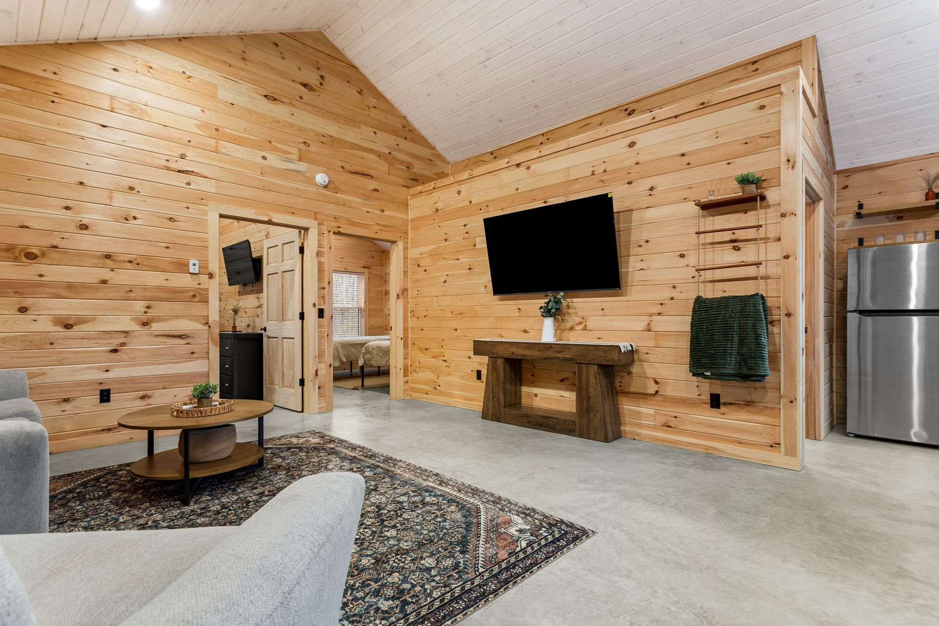 Cozy living room with wood-paneled walls, white sofa, jute rug, and dining table by a window.