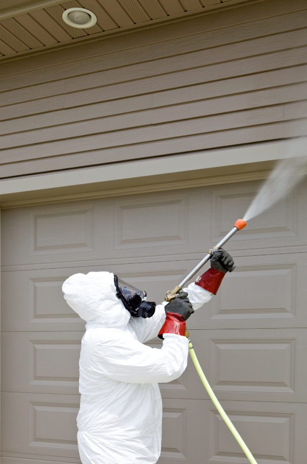 Pest control worker spraying insecticide on a home's garage.