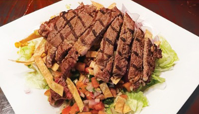 Steak salad on a white plate: grilled steak slices atop lettuce, salsa, and tortilla strips.