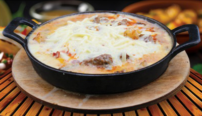 Baked dish with cheese topping in a black cast iron skillet, on a wooden board.
