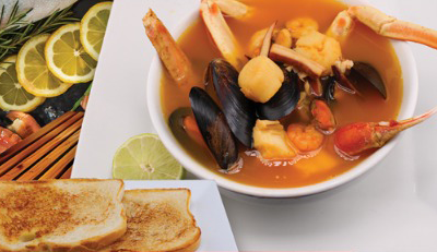 Seafood stew in a white bowl, with mussels, crab legs, and shrimp.