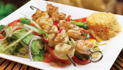 Grilled seafood skewers with rice and salad on a white plate.