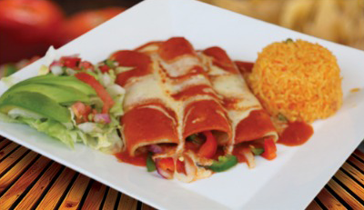 Enchiladas with red sauce, rice, avocado, and salad on a white plate. Enchiladas with red sauce, rice, avocado, and salad on a white plate.