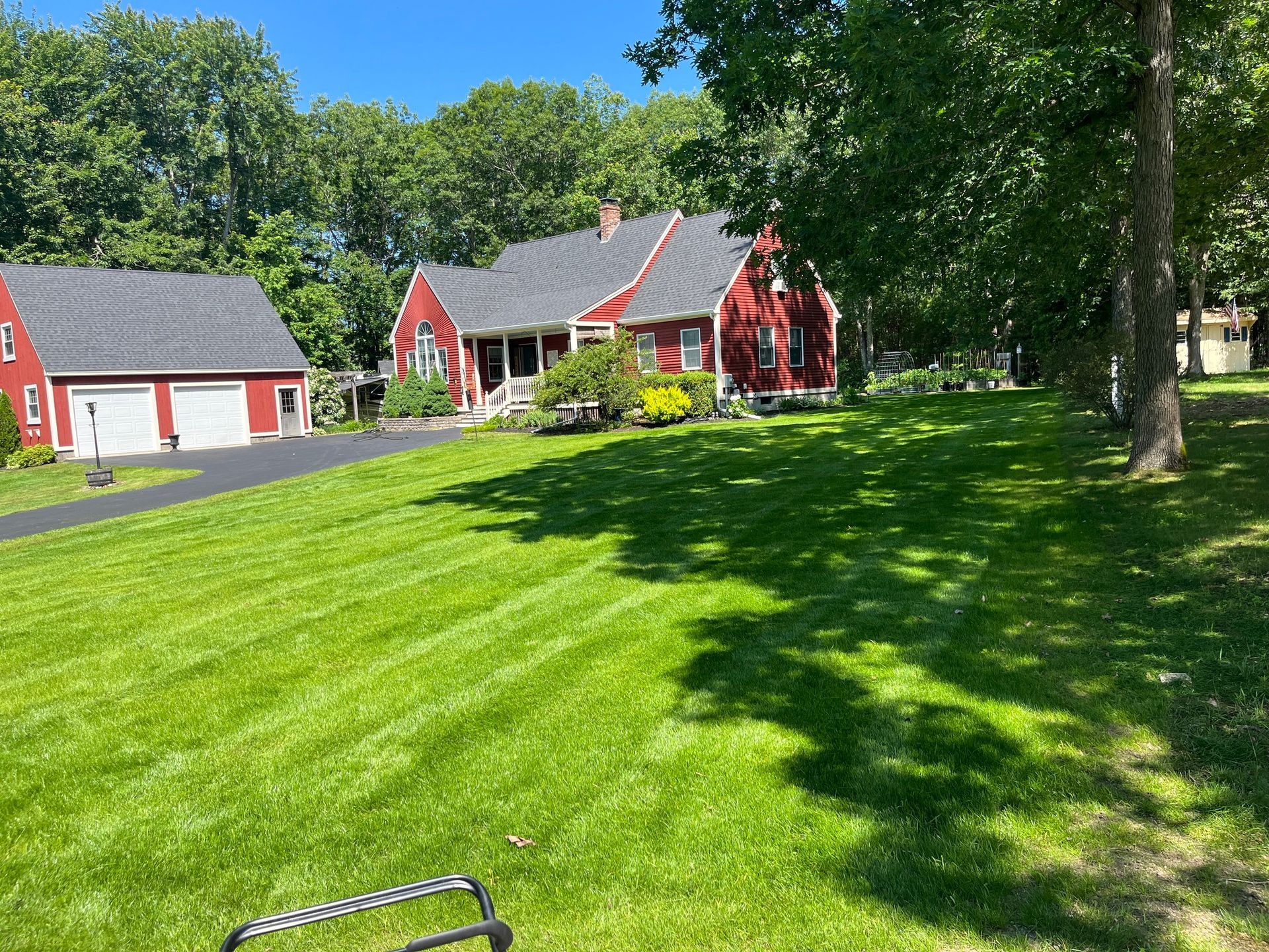 Red house and detached garage with freshly mowed green lawn and trees.