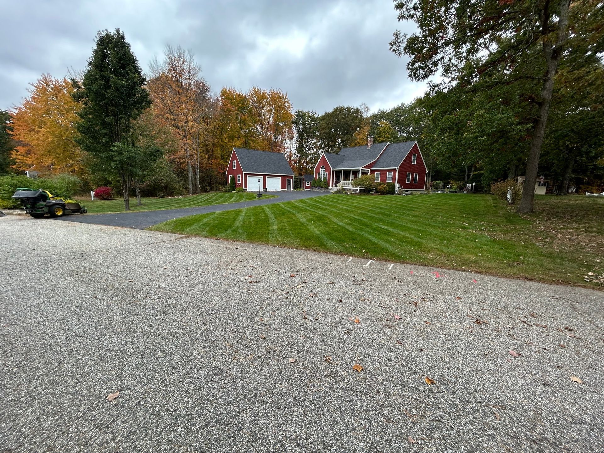Red house and garage with fresh-cut green grass and fall foliage under a cloudy sky.