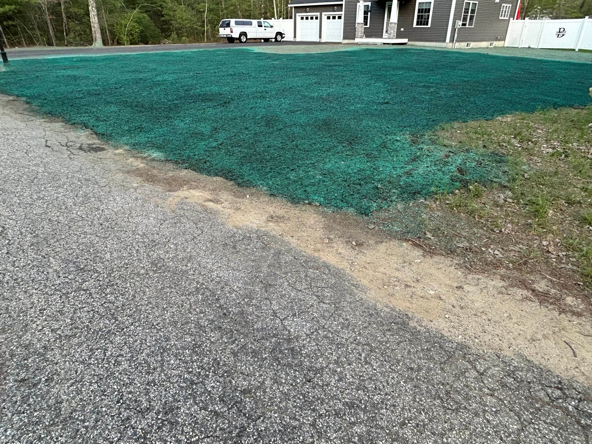 A green-covered lawn next to a driveway and a house with a white garage.