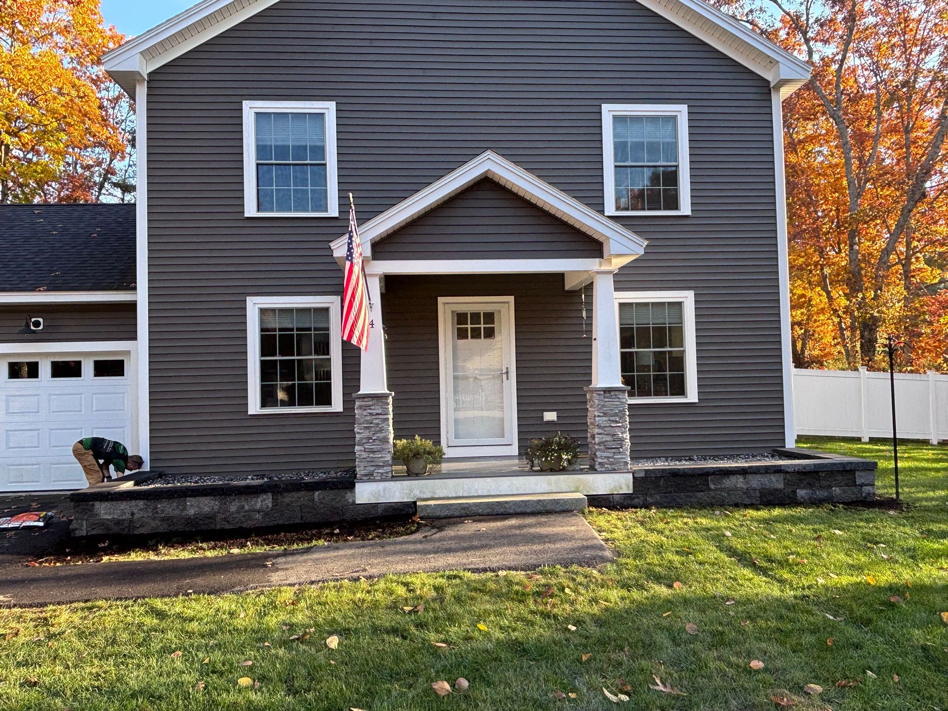 Two-story gray house with white trim. Porch with stone columns and an American flag.