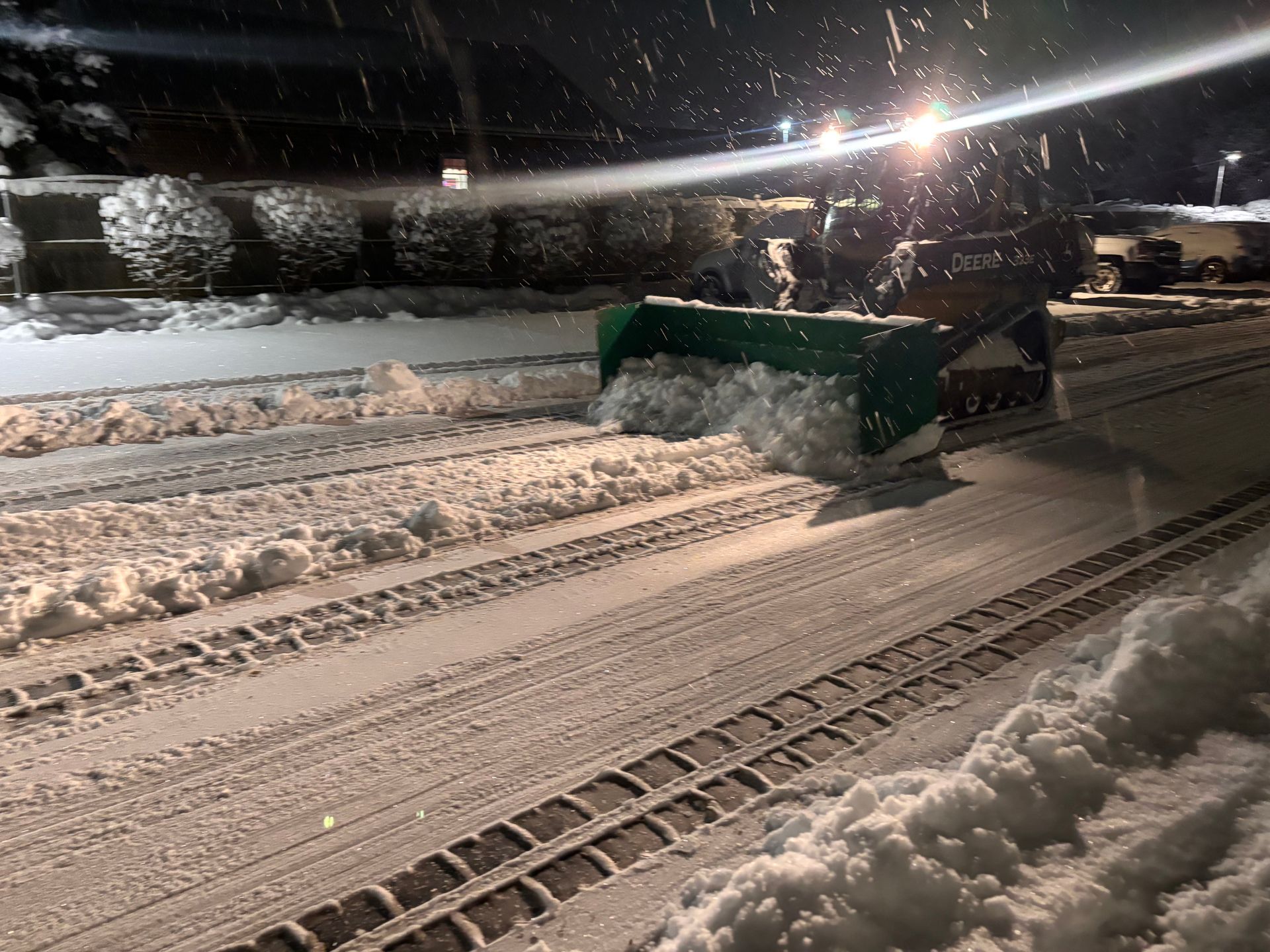 Snowplow clearing snow from a road at night. Green plow pushes snow aside.