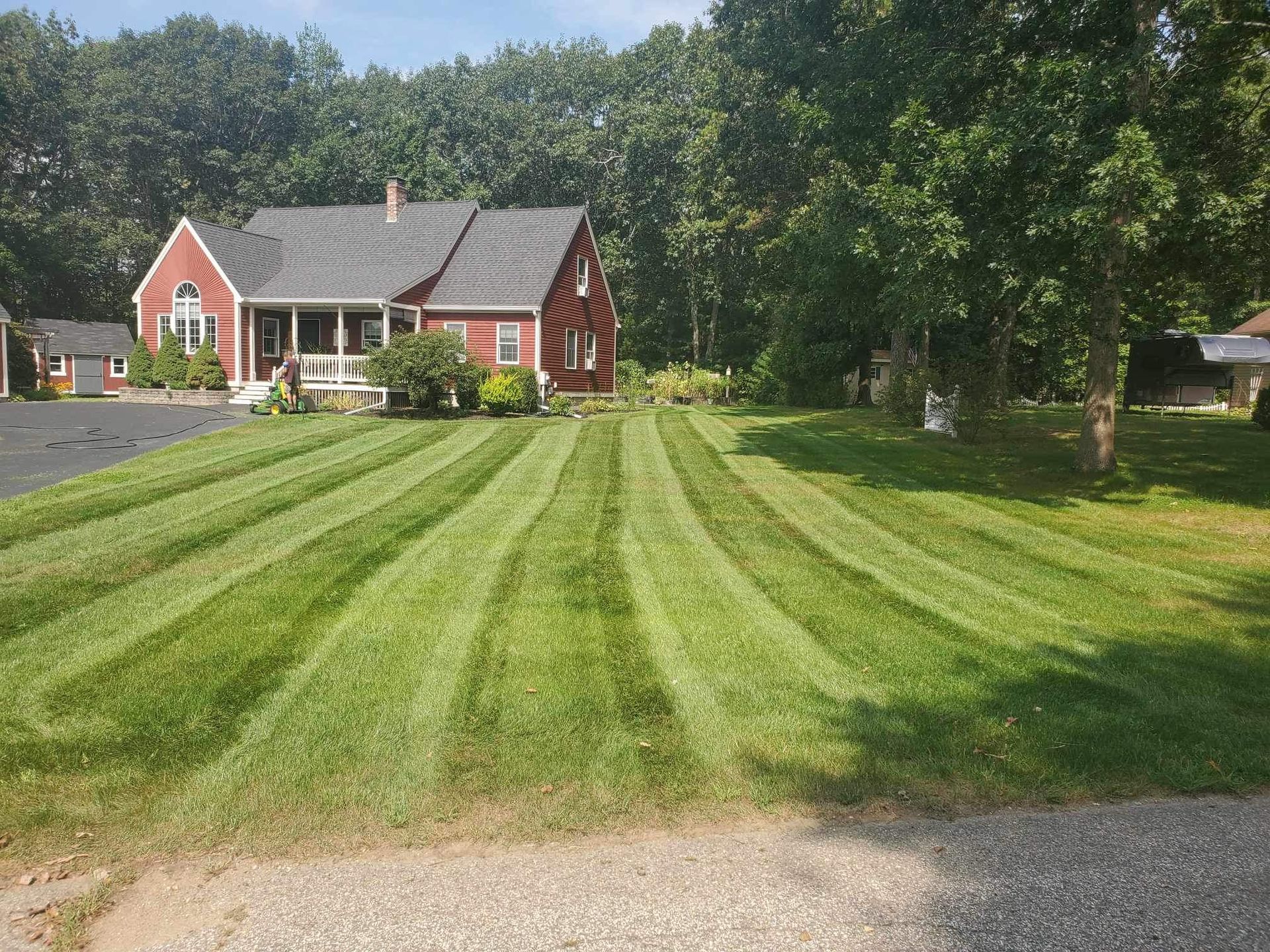 Red house with striped lawn, blue sky, trees in the background.