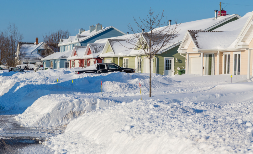 Man shoveling snow from a driveway next to a car and house on a snowy day.