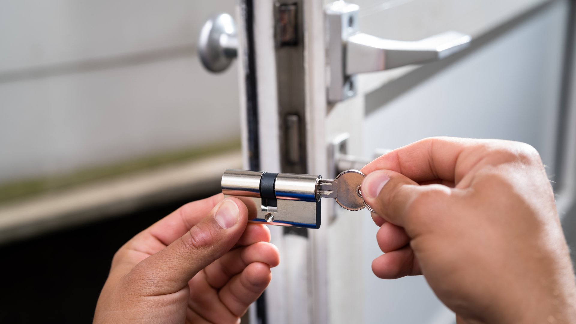 Person inserting a key into a silver door lock cylinder on a white door.