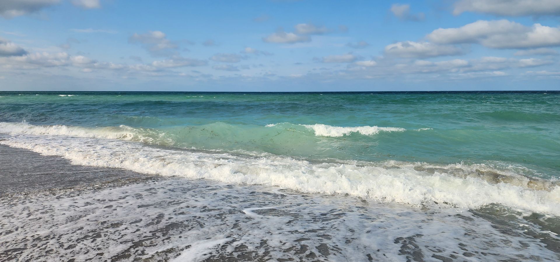 Waves washing onto a pebbly beach under a blue sky and turquoise sea