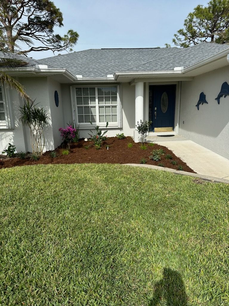 Single-story house with blue front door, white exterior, and landscaped front yard under a sunny sky