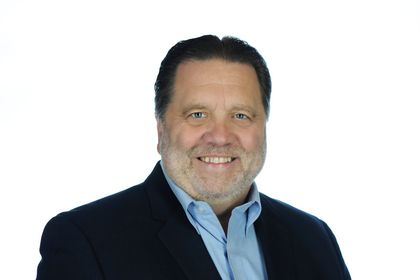 Headshot of a smiling man in a dark jacket and light blue shirt against a white background