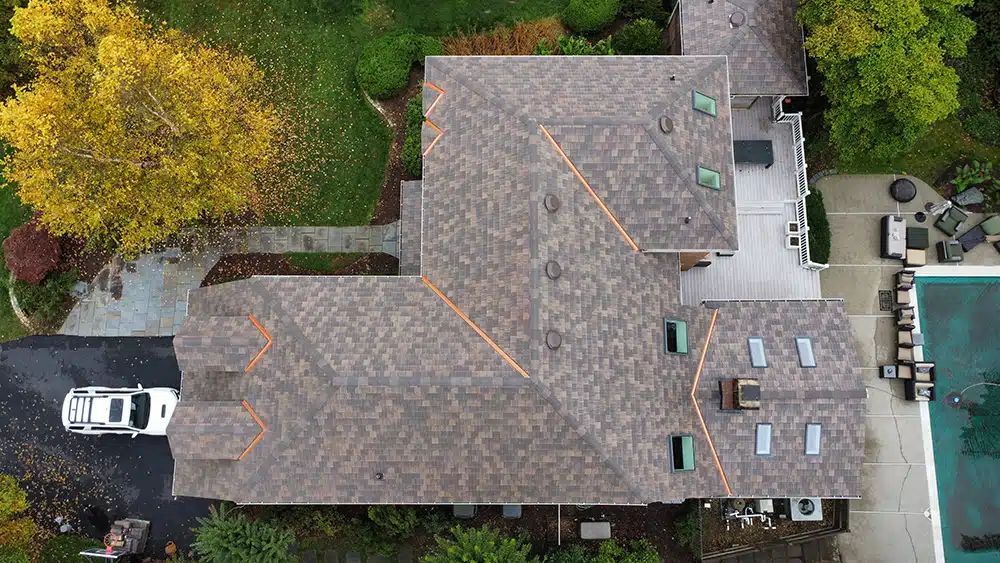 Overhead view of a house with a brown roof, a driveway with a white car, and a pool.