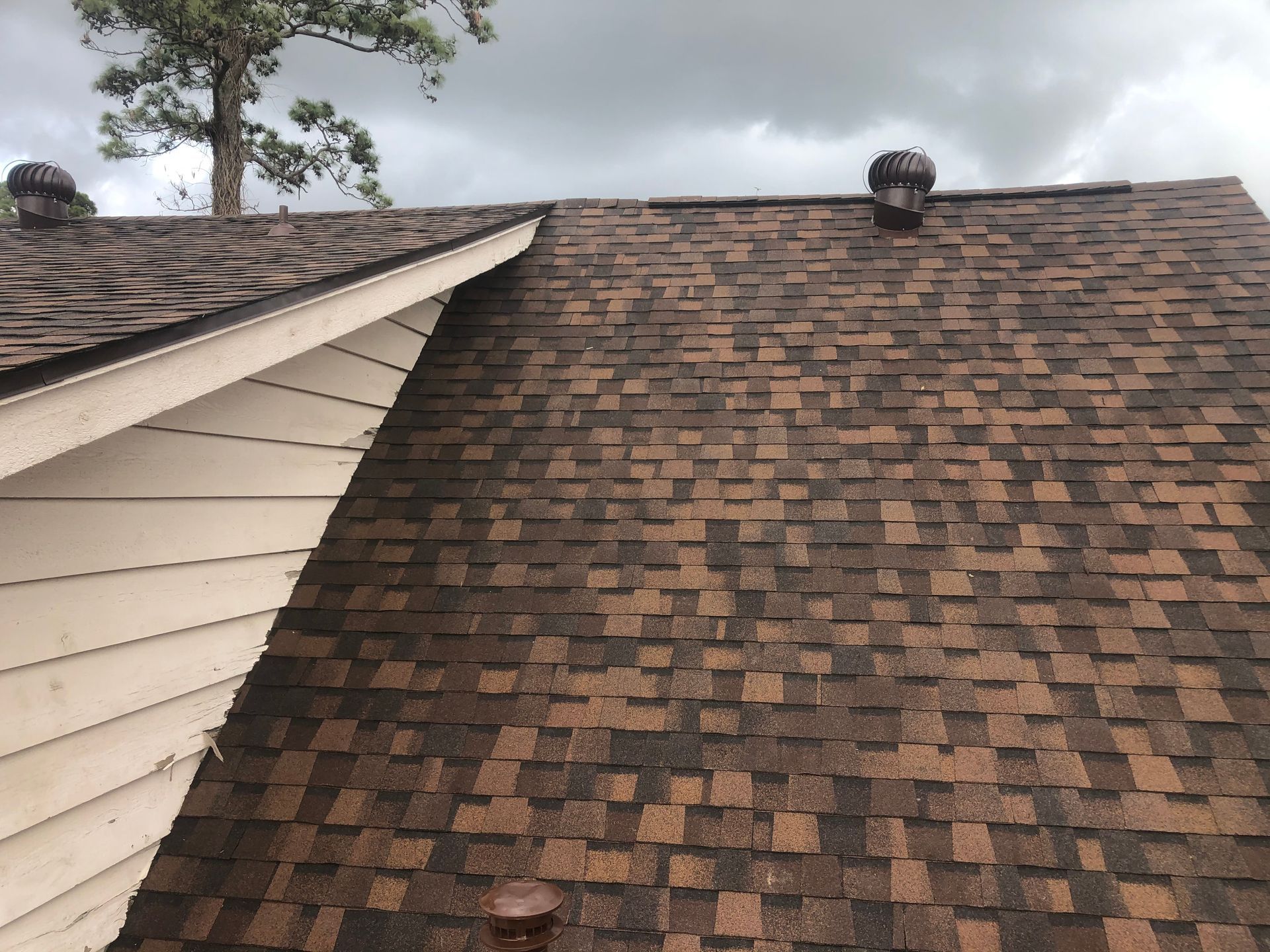 A brown asphalt shingle roof with two vents and a white trim, against a cloudy sky.