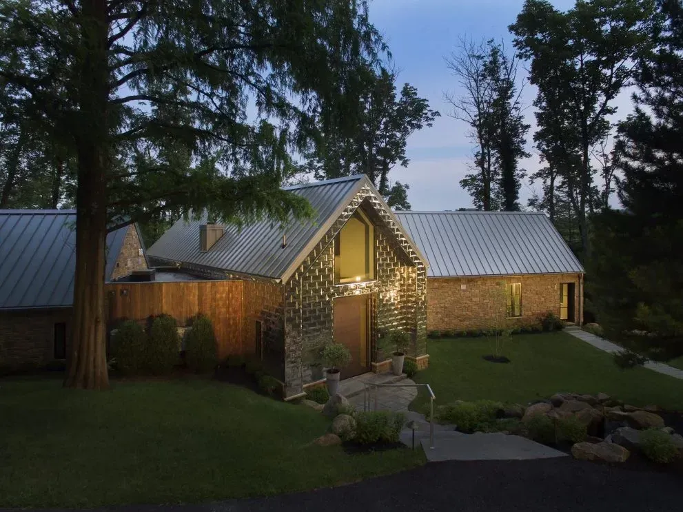 A brick house with a metal roof is surrounded by trees
