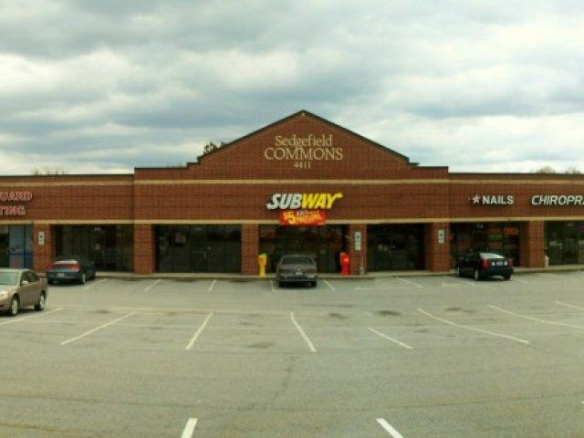 Several cars are parked in front of a subway restaurant