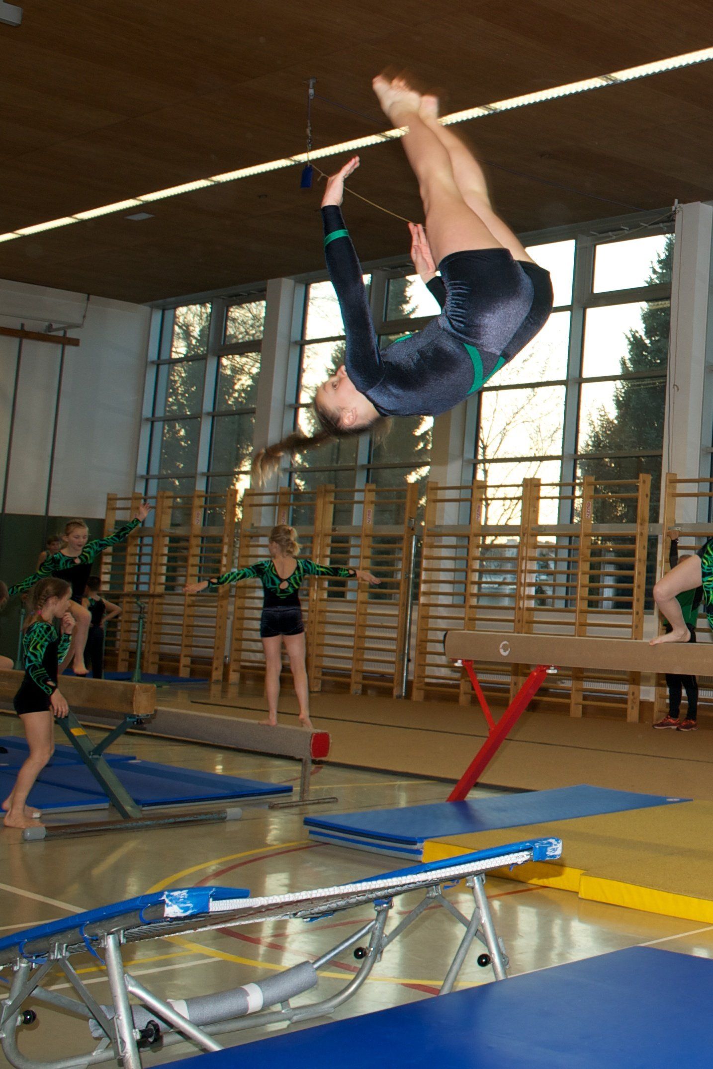 Eine Turnerin macht in einer Turnhalle einen Handstand auf einer Reckstange.