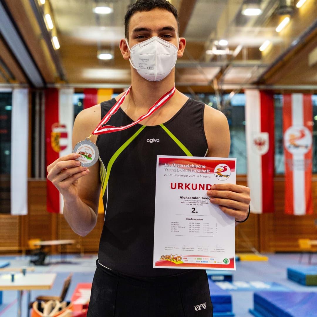 Ein Mann mit einer Maske hält eine Urkunde und eine Medaille