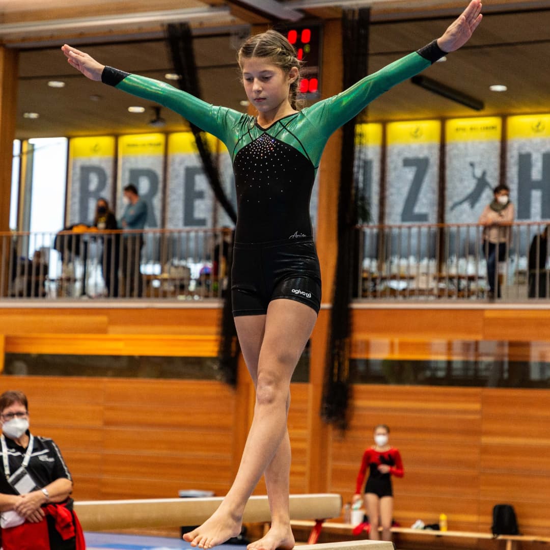 Eine Turnerin steht mit ausgestreckten Armen auf einem Schwebebalken