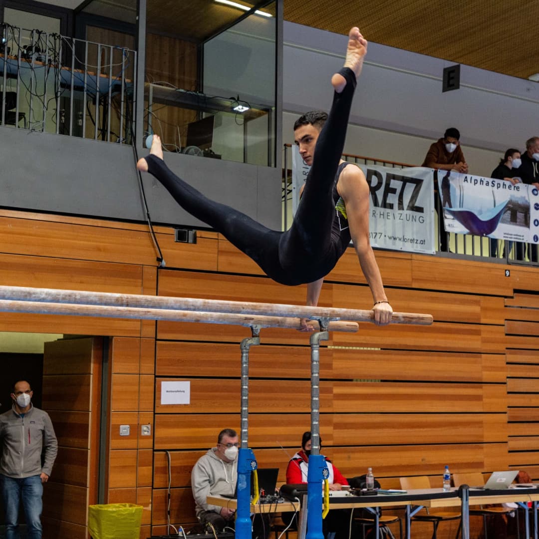 Ein Mann macht einen Spagat an einem Barren vor einem Schild mit der Aufschrift „RFTZ“