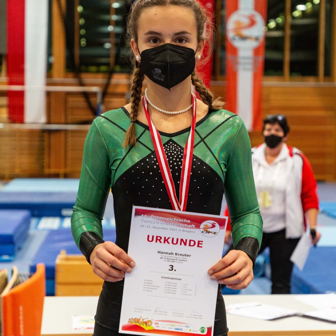 Eine Frau mit einer Maske hält ein Zertifikat mit der Aufschrift „Urkunde“ in der Hand